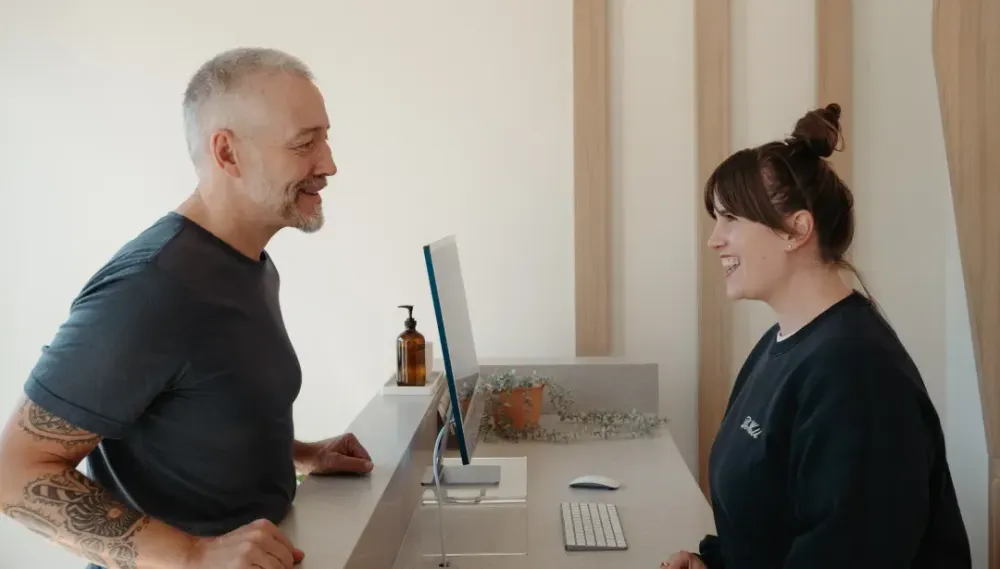 Front desk practitioner greeting a patient with a warm smile during check-in, creating a memorable patient experience.