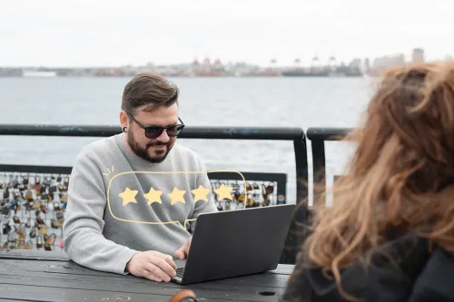 A practitioner is on his laptop on a picnic table with the ocean in the background and illustrated gold stars popping up from a speech bubble on the laptop