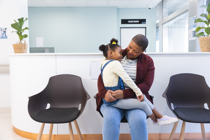 A young girl smiles as she sits in her parent's lap in a waiting room