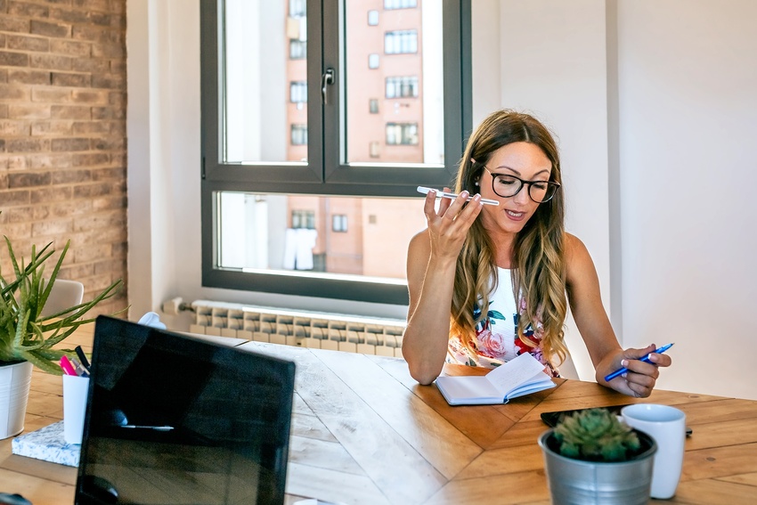 A woman speaks on the phone while looking at her notebook on her desk