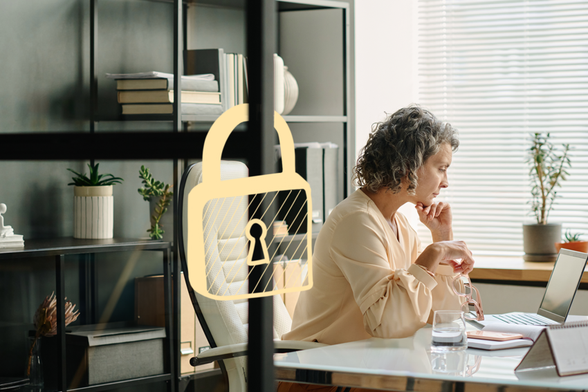 A woman stares at her laptop in her office with a serious expression, her glasses in her hands. She wears her hair in curls and has a peach top on. There is an illustration of a lock around her office door.