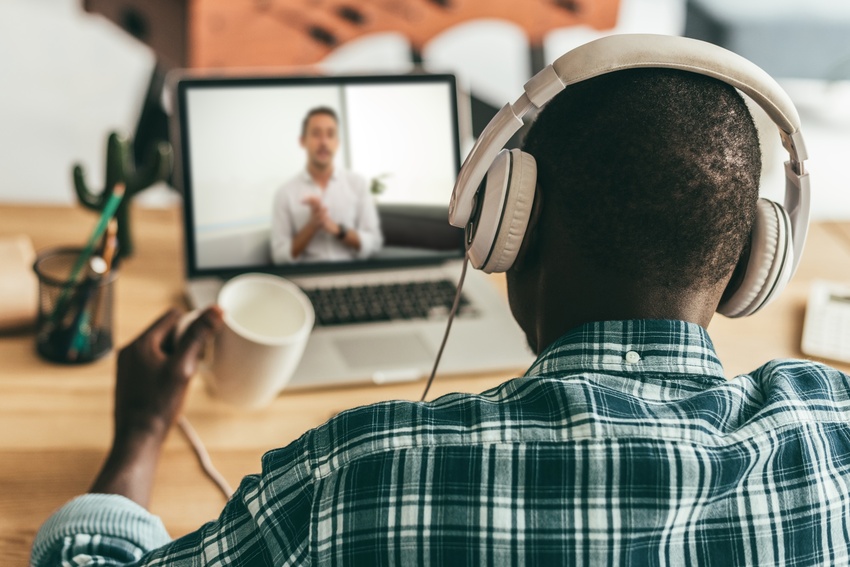 A client meets with their therapist over telehealth on a laptop. The client wears headphones and has a mug in their hand while their therapist talks.